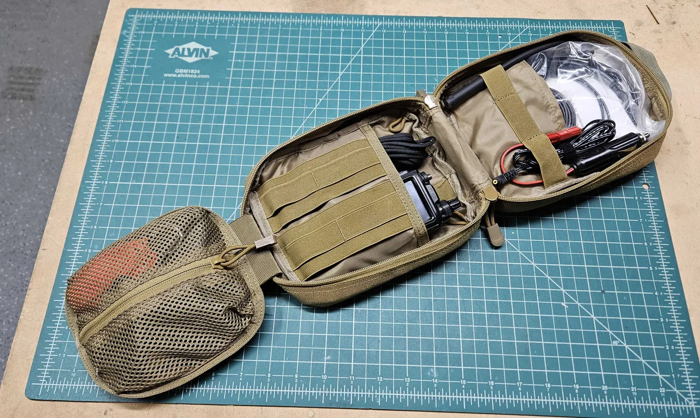The open tan MOLLE pouch lying flat, with the radio, the chargers and the coiled cables in separate pockets and a mesh pouch on the left