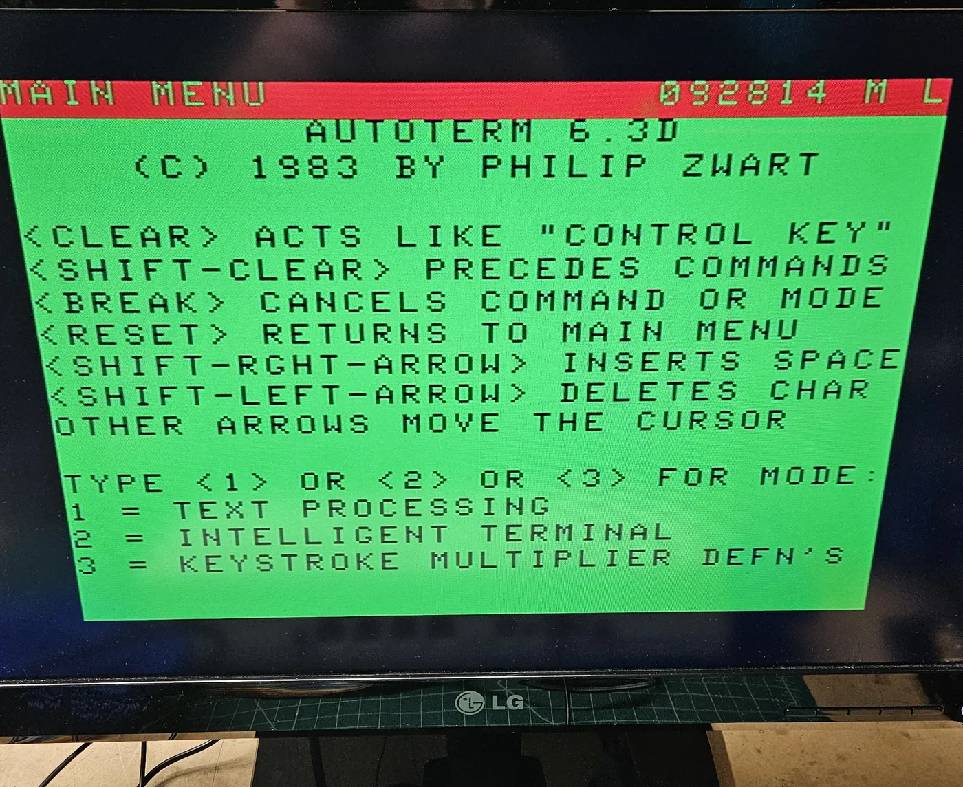 The monitor showing the AutoTerm main menu in black text on the classic green Color Computer screen