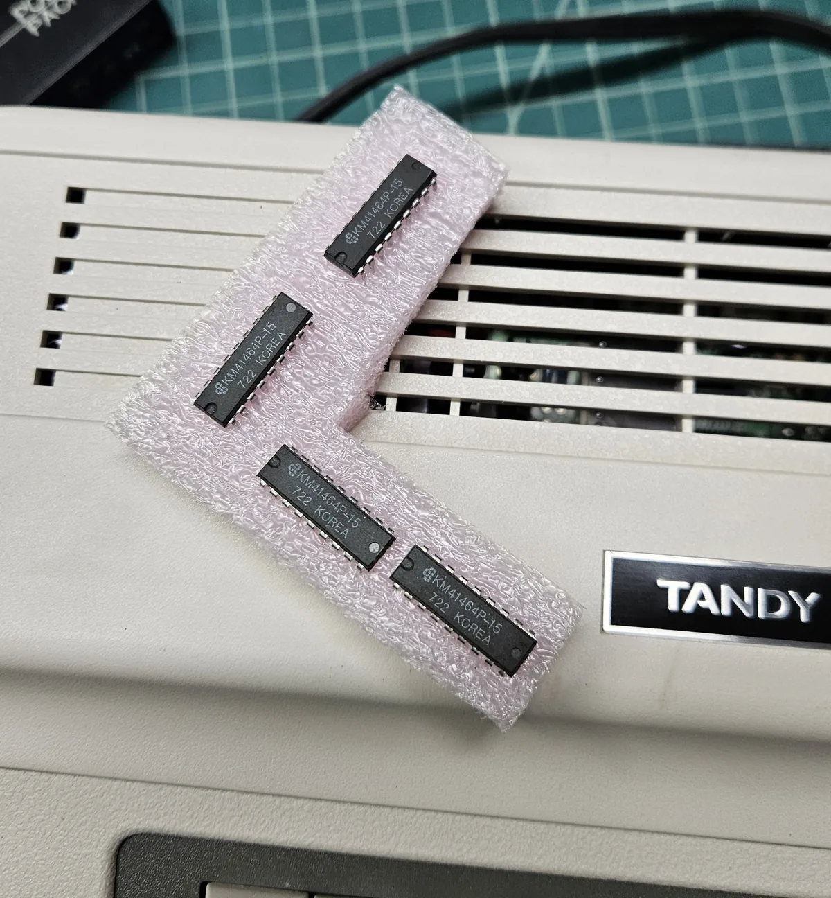 Four small memory chips pressed into pink anti-static foam, resting on the computer's case