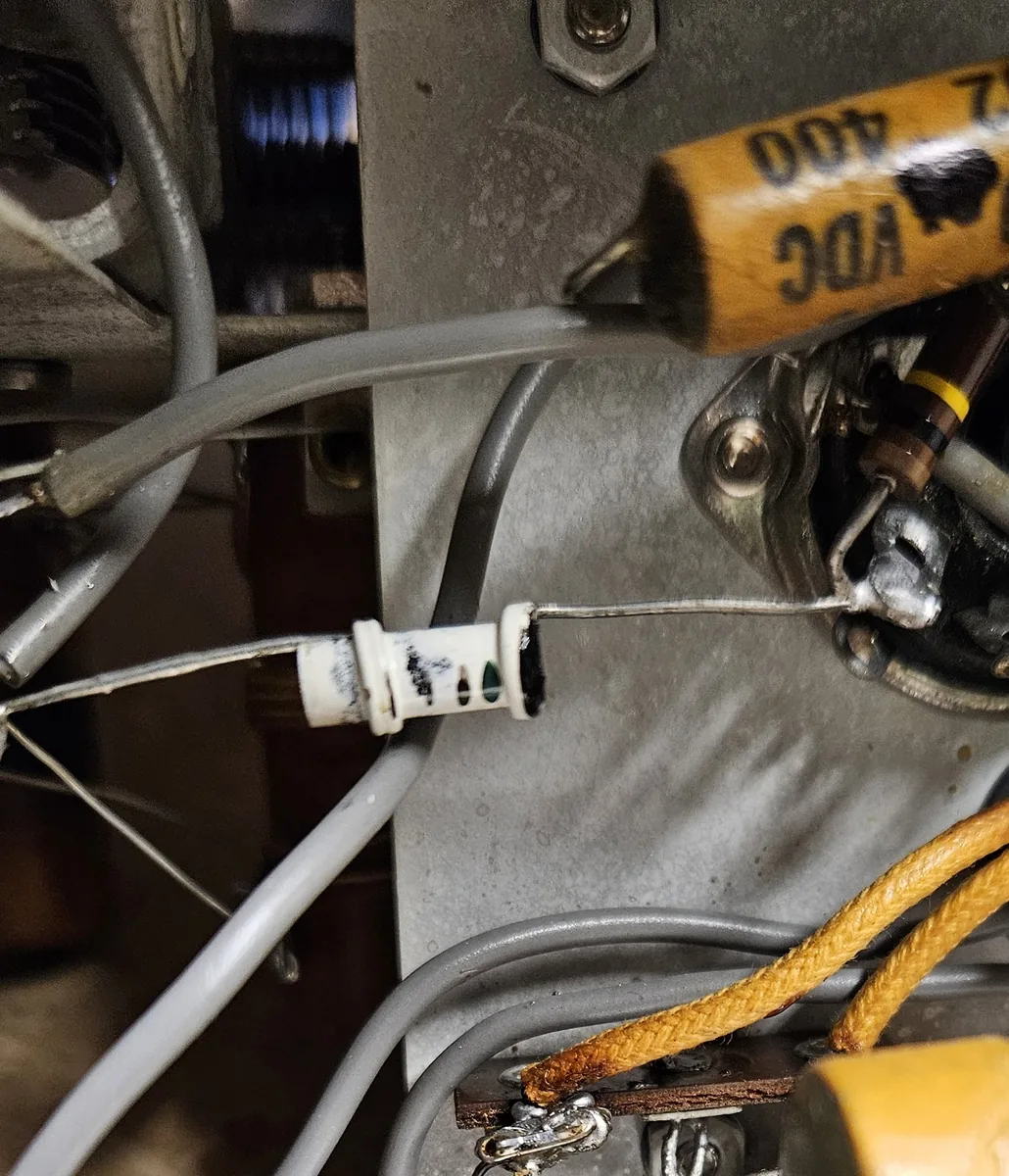 A small white cylinder with wire leads soldered between a tube socket and the band switch, next to an old yellow wax capacitor