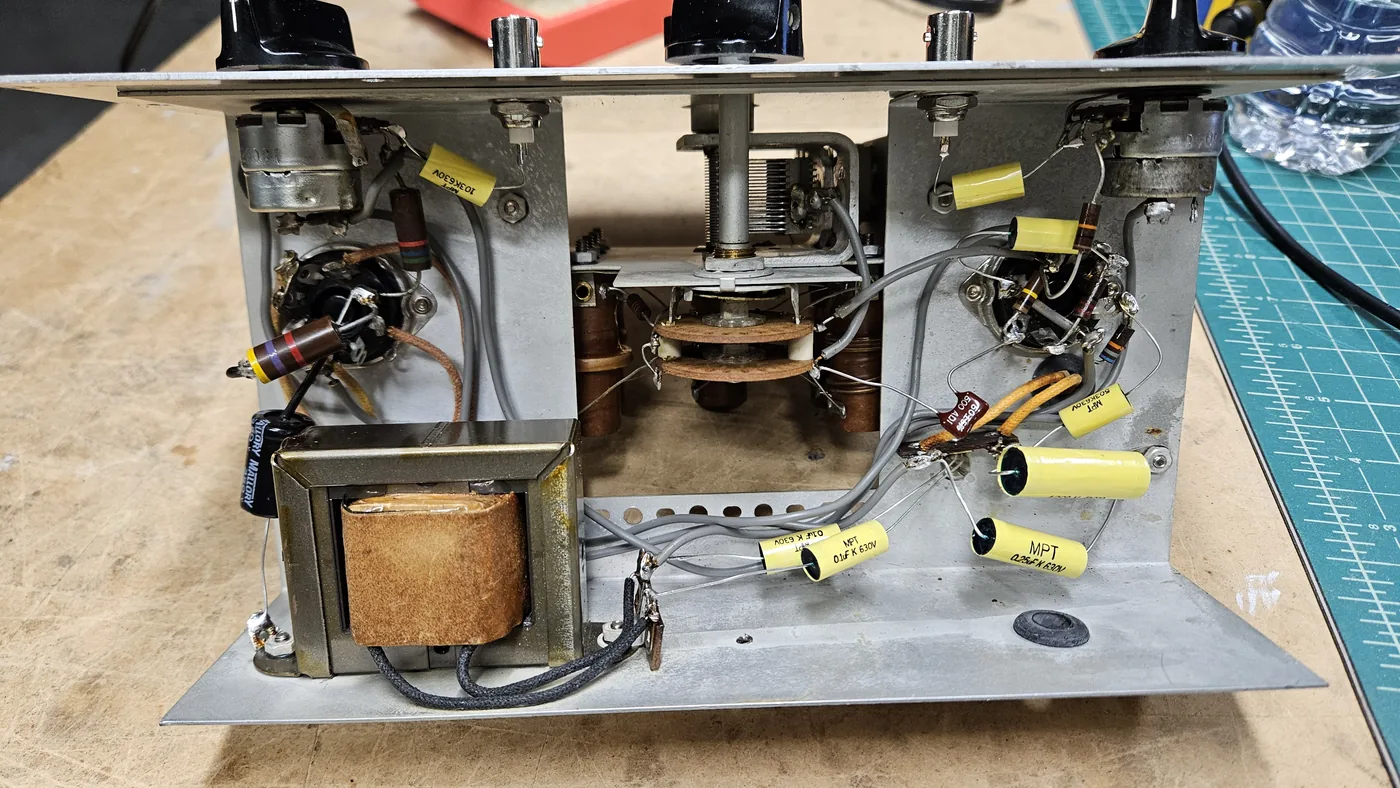 The underside of the chassis after the work, with bright yellow film capacitors, a small red mica capacitor and a black electrolytic capacitor wired in where the old parts were