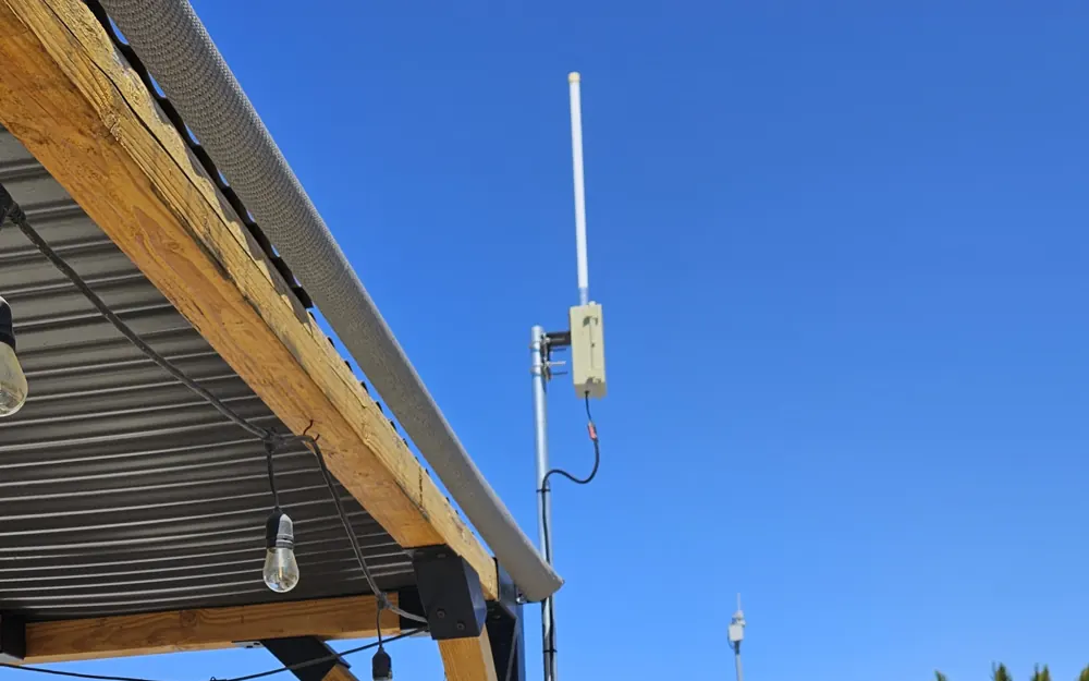 White fiberglass antenna on a metal pole beside a patio cover, with a small tan weatherproof box just below it