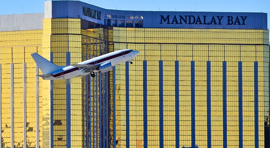 A white Janet Boeing 737 with a red stripe climbing past the gold Mandalay Bay tower in Las Vegas
