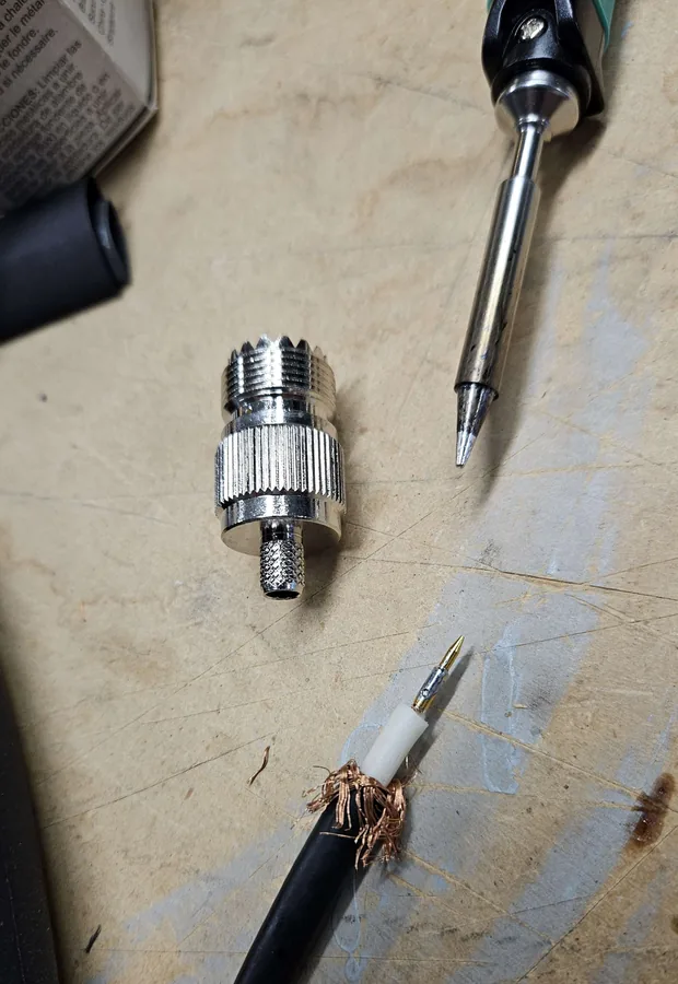 A UHF connector and the prepared end of the coax on the bench beside a soldering iron