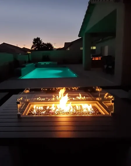 The pool glowing aqua at dusk, seen past a lit fire pit table on the patio