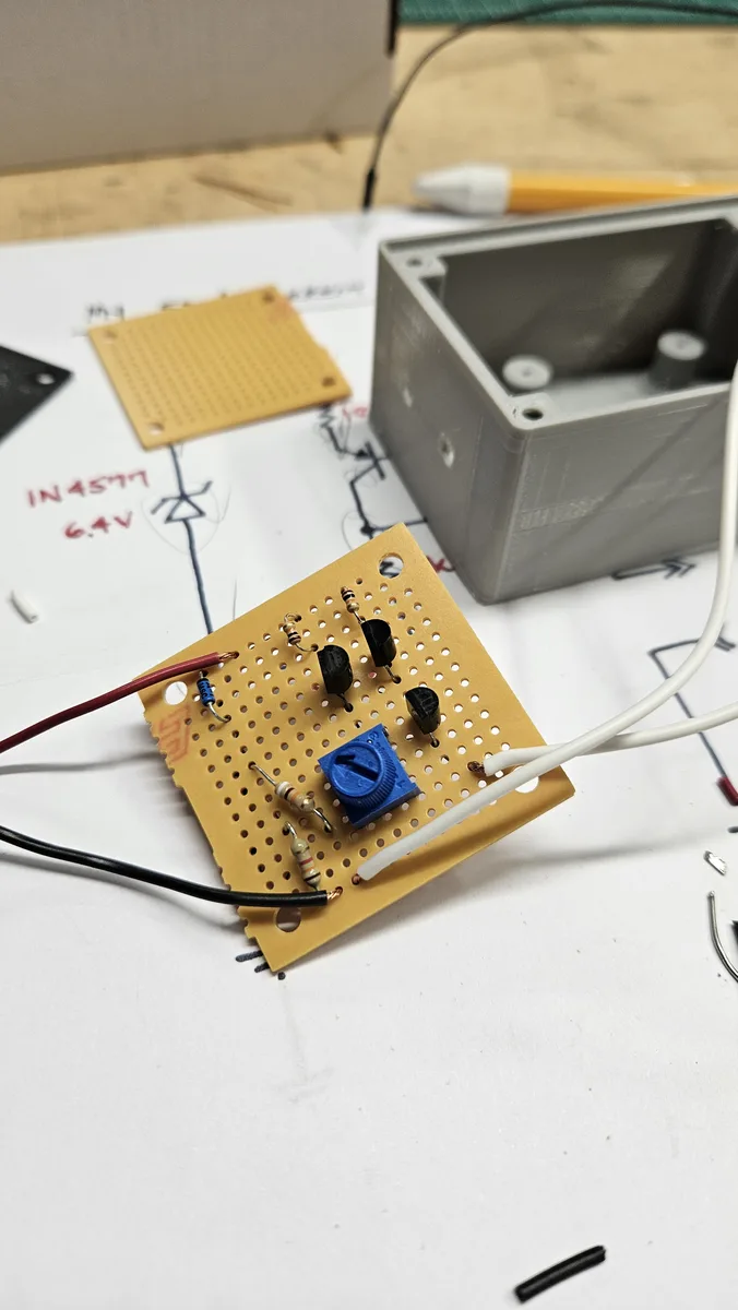 The perfboard version of the circuit, with transistors and a blue trimmer, next to a gray plastic box